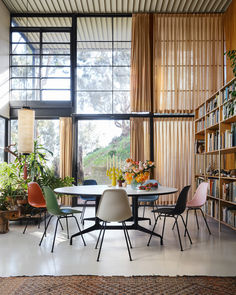 a dining room table with chairs and bookshelves in front of large open windows