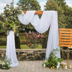 an outdoor wedding setup with white drapes and greenery on the side walk way