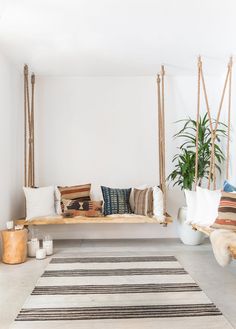 a wooden bench with pillows on it in front of a potted plant and rug