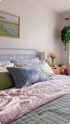 a bed with pillows and blankets in a bedroom next to a plant on the window sill