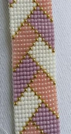 a pink and white cross stitched tie with gold beads on it's end