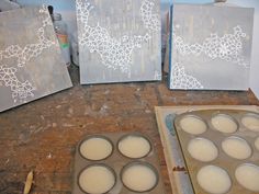 some cupcake pans sitting on top of a table next to two canvases