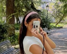 a woman is taking a photo with her cell phone while sitting on a park bench