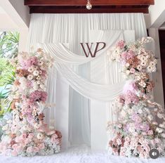 the wedding arch is decorated with pink flowers and white drapes, along with monogrammed letters