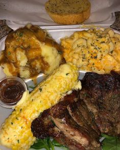 a plate with steak, macaroni and cheese on it next to some bread