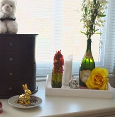 a white stuffed animal sitting on top of a dresser next to flowers and bottles in front of a window