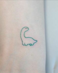 a small green dinosaur tattoo on the left side of the arm, which is drawn in blue ink