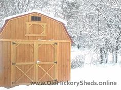 a barn in the middle of winter with snow on the ground and trees behind it