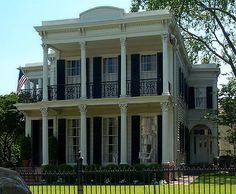 a large white house with black shutters and an american flag on the front porch