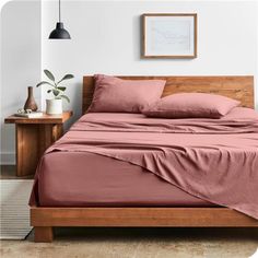 a bed with pink sheets and pillows in a white room next to a wooden table