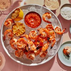 a plate with shrimp, lemon wedges and sauce on it next to other dishes