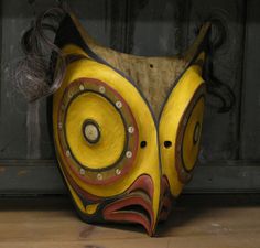 a yellow and red mask sitting on top of a wooden floor next to a wall