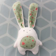 a white stuffed animal with pink flowers on it's face and ears, sitting in front of a gray background