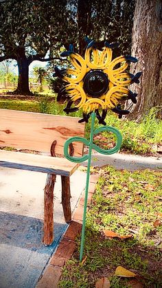 a sunflower sitting on top of a wooden bench next to a tree and grass