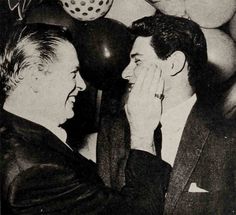 black and white photograph of two men talking to each other in front of balloon decorations