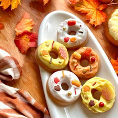 several donuts are arranged on a white platter with autumn leaves and pumpkins in the background