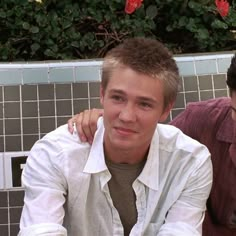 two young men sitting next to each other in front of a wall with flowers on it