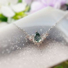 a green bird necklace sitting on top of a white plate with flowers in the background