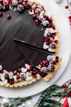 a chocolate tart decorated with pomegranates and cranberries on a white plate