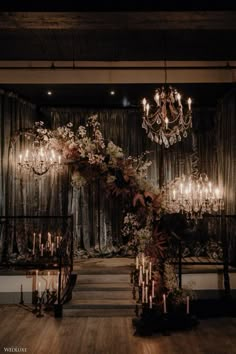 an elegant wedding setup with chandeliers and flowers on the wall, candles in the center