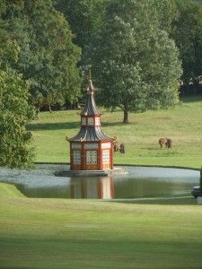 a gazebo sits in the middle of a pond with horses grazing on the other side