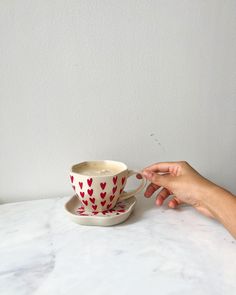 someone is holding onto a cup on a saucer with hearts painted on the side