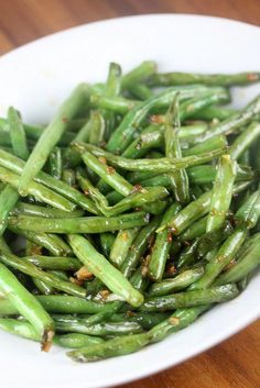 a white bowl filled with green beans on top of a wooden table