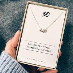 a person holding up a box with a necklace in it that reads 30 celebrating 3 decades