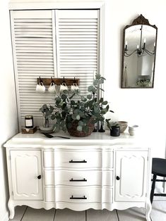 a potted plant sitting on top of a white dresser next to a mirror with shutters