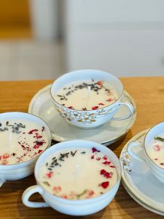 four cups and saucers filled with soup on top of a wooden table next to a plate