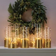 gold candles are lined up in front of a wreath on top of a mantel