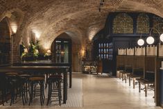 a bar with stools and tables in an old brick walled area, lit by lamps