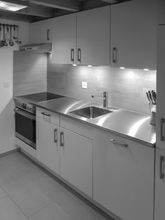 a black and white photo of a kitchen with stainless steel sink, cabinets, and counter tops