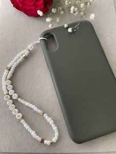 the phone case is next to a flower and beaded necklace on a gray surface