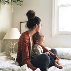 a woman sitting on top of a bed holding a baby