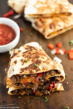 two quesadillas cut in half on a wooden table with sauce and peppers