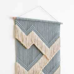 a wall hanging made with yarn and tassels on a white wall next to a wooden stick