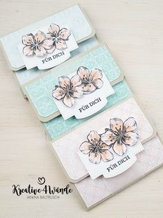 three cards with flowers on them sitting on top of a wooden table next to each other