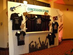 an exhibit booth with t - shirts and guitars on the wall, in front of a curtain