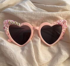 ITEM DETAILS *Heart shaped custom sunglasses in pink or white *Each pair is handcrafted and can accommodate any special requests or names you would like reflected. *Standard design will be Cherry and rhinestone decoration or rhinestone heart decoration. *Pink glasses in picture are reflecting the Cherry decoration +White glasses in picture are reflecting the Heart rhinestone decoration. Pink Fun Sunglasses With Glass Lenses, Fun Pink Glass Sunglasses, Playful Personalized Pink Sunglasses, Pink Plastic Sunglasses As Gift, Personalized Pink Sunglasses For Beach, Fun Pink Sunglasses For Gift, Pink Personalized Adjustable Sunglasses, Customizable Pink Sunglasses For The Beach, Pink Tinted Sunglasses As Gift