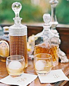 two wine glasses sitting on top of a wooden table next to bottles and glassware