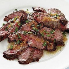 a white plate topped with sliced steak covered in sauce and garnished with parsley