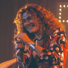 a man with long curly hair is smiling and holding a microphone in his right hand