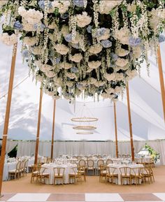 an outdoor tent with tables and chairs set up for a wedding reception under a floral chandelier