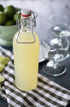 a bottle of lemonade sitting on top of a table next to glasses and limes