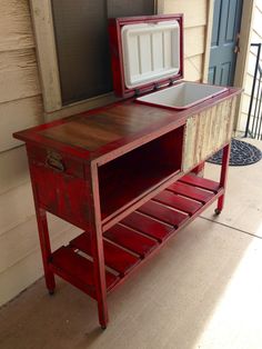 an old red table with a cooler on it's top and some drawers underneath