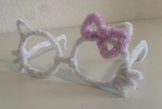 two knitted cat ears are sitting on a table top, one is pink and the other is white