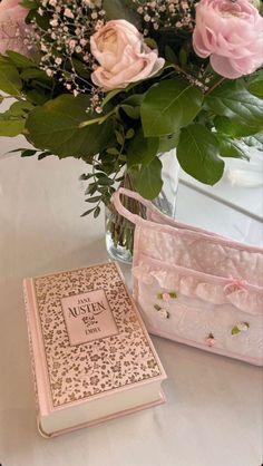 a vase filled with pink flowers next to a book on top of a white table