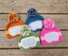 three crocheted hats with pom - poms on them sitting on a wooden surface