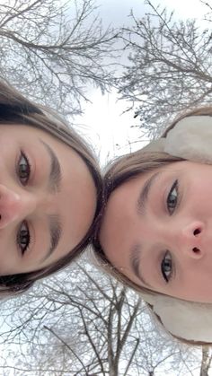 two girls are looking up at the camera with trees in the background and snow on the ground